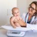 A baby boy sitting on scale during weight measuring exam at doctor office. Pediatrician weighting baby girl on scales