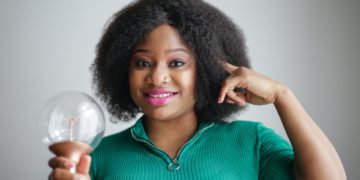 A black woman holds a light bulb with her finger on her head