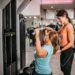 Senior woman doing lat pulldowns exercise in gym with trainers help
