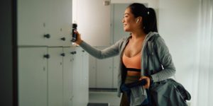 Happy athletic woman taking her stuff from a locker after finishing sports training in a gym.