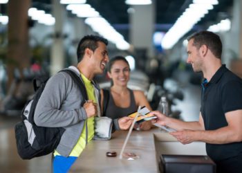 A happy couple at the gym discussing membership options with the receptionist - healthy living principles