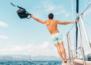 A man wearing white shorts holding black backpack