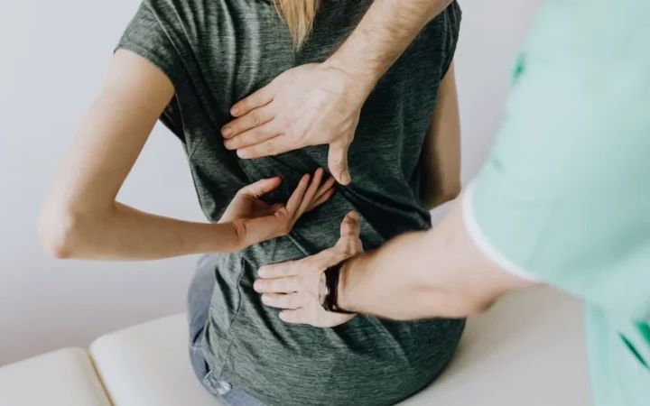 From above of crop faceless slim female patient sitting on examination couch and indicating osteopath in uniform pain spot