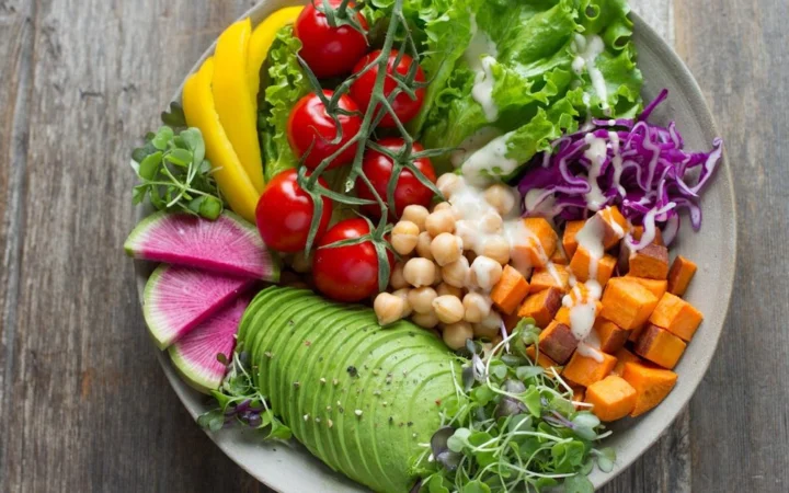 A bowl of salad with avocado, chickpeas, tomatoes and radish on a wooden table