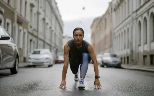 Woman in activewear poised for a run on a city street, symbolizing fitness and determination.