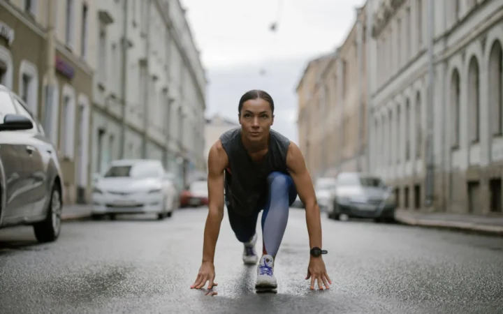 Woman in activewear poised for a run on a city street, symbolizing fitness and determination.