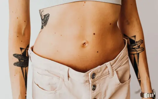Close-up of a tattooed woman's torso wearing high-waisted pants, showcasing body art and style.