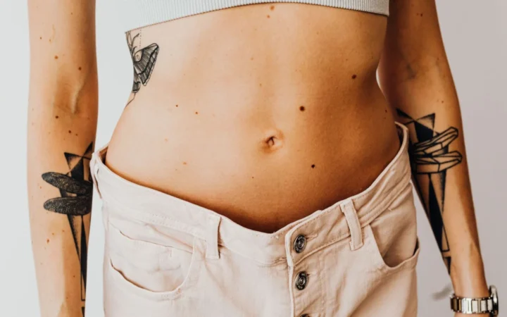 Close-up of a tattooed woman's torso wearing high-waisted pants, showcasing body art and style.