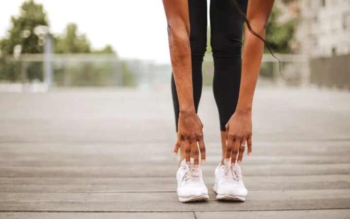 From below crop slender female athlete in sportswear and white sneakers doing standing forward bend exercise for stretching