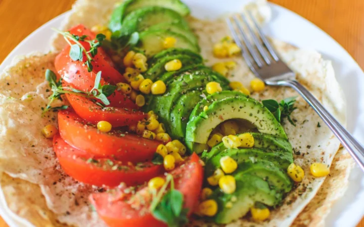 Vibrant salad with avocado, tomato, and corn on flatbread, topped with herbs, perfect for a healthy meal.