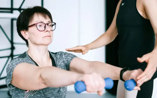 Personal trainer guides a woman in exercising with dumbbells for fitness and strength training.