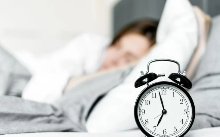Retro alarm clock sits by a sleeping woman in a cozy bedroom setting.