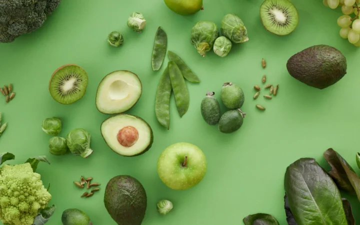 Variety of fresh green fruits and vegetables on a matching background, showcasing healthy organic produce.