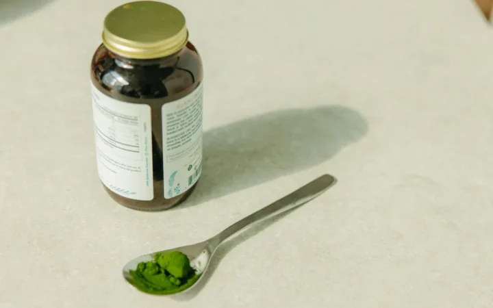 Close-up of a jar and a spoon with green powder, ideal for healthcare and wellness themes.
