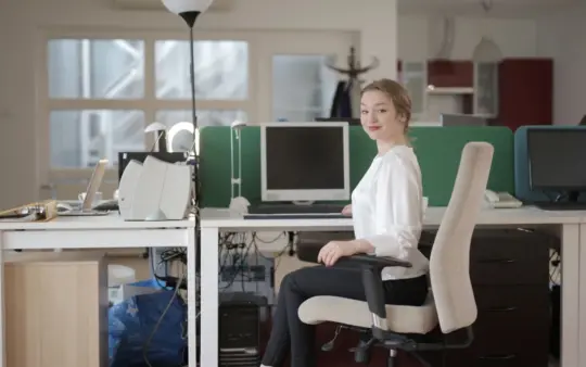 Side view of glad female worker in classy outfit sitting at table on office chair during work in modern workplace and