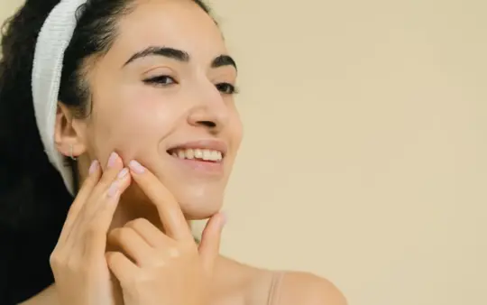 Close-up of a smiling woman applying skin treatment, promoting natural beauty and skincare.