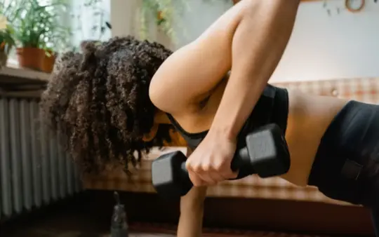 African American woman working out with dumbbells in an indoor setting, promoting a healthy lifestyle.