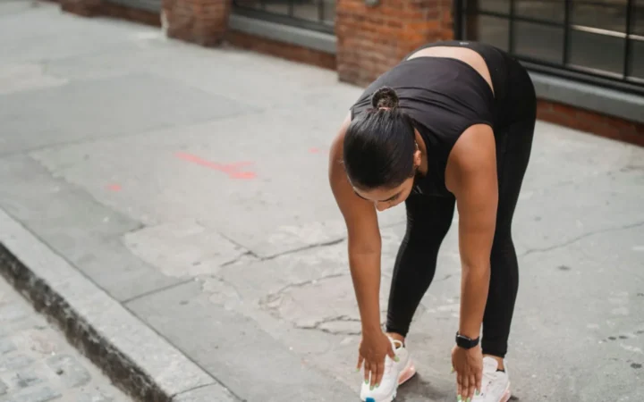 Woman in athletic wear performs stretching exercises on a city sidewalk, promoting a healthy lifestyle.