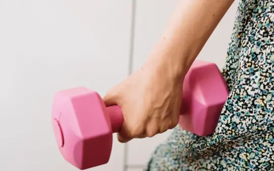 Close-up of a woman's hand holding a pink dumbbell, symbolizing fitness and strength.