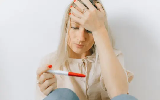 Concerned woman looks at a pregnancy test, reflecting emotions of anxiety and uncertainty.