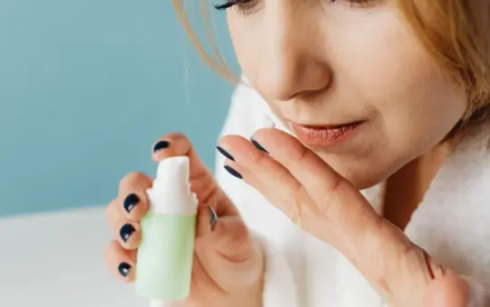 Close-up of a woman in a bathrobe applying skincare cream, focusing on self-care and beauty routine.