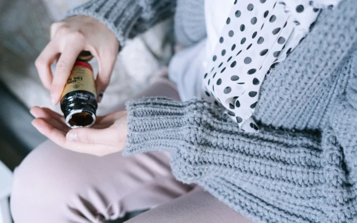 Close-up of a woman in cozy clothing holding a medicine bottle in her hands.