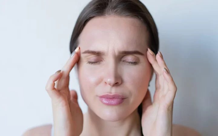 Close-up of a woman with closed eyes holding her temples, showing signs of a migraine or headache.