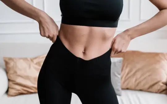Close-up of a woman in activewear adjusting her pants in a stylish living room.