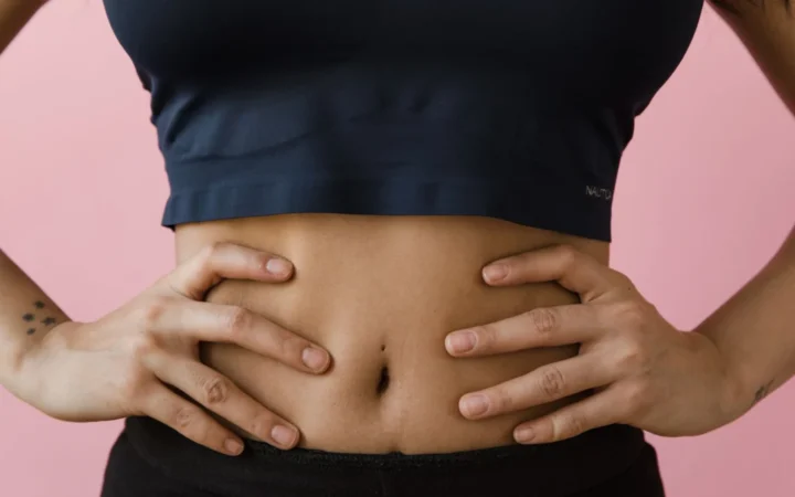 Close-up shot of a woman's toned stomach with hands on hips, against a pink background.
