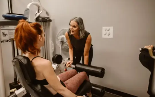Personal trainer guiding women during a workout session in a gym setting.