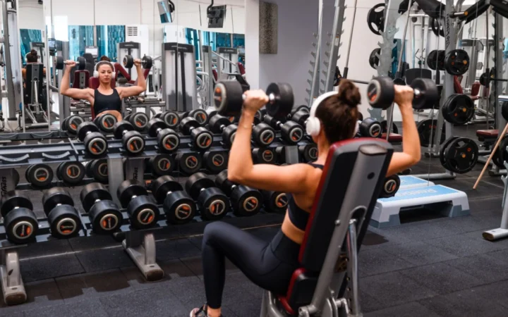 Woman exercising in the gym lifting dumbbells with headphones on for a strength-building workout.