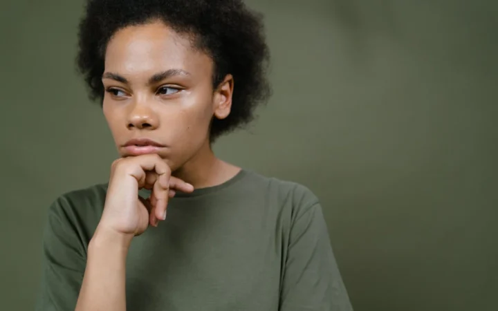 Pensive young woman with afro hair contemplating and looking away, emphasizing individuality and emotion.