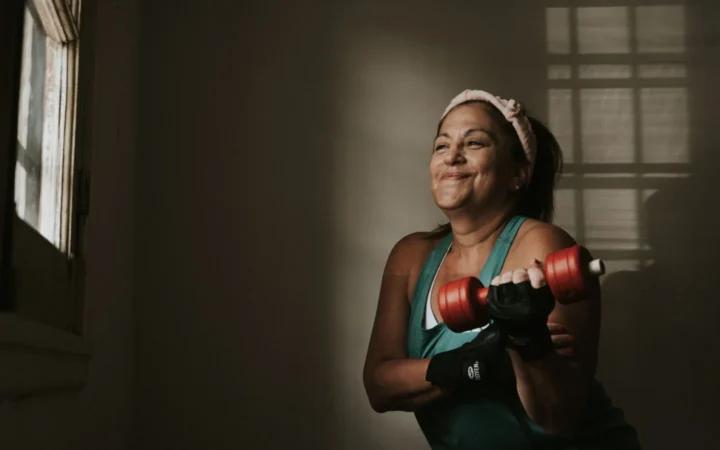 Confident middle-aged woman lifting dumbbells indoors, embracing a healthy lifestyle.