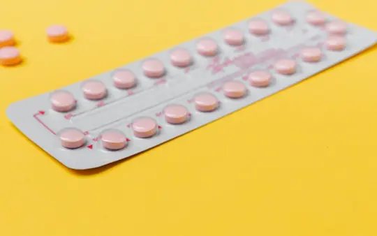 Blister pack of pink pills placed on a vibrant yellow background, symbolizing medicine and healthcare.