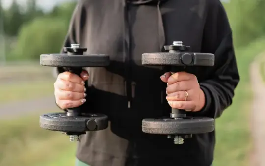 Close-up of a woman holding dumbbells outdoors, focusing on fitness and strength training.