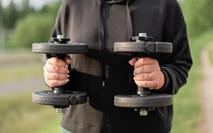 Close-up of a woman holding dumbbells outdoors, focusing on fitness and strength training.