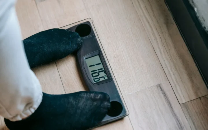 From above of unrecognizable person in socks standing on electronic weighing scales while checking weight on parquet during