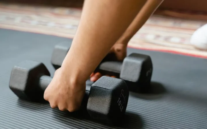Close-up of a person picking up dumbbells on a yoga mat, emphasizing fitness and exercise.