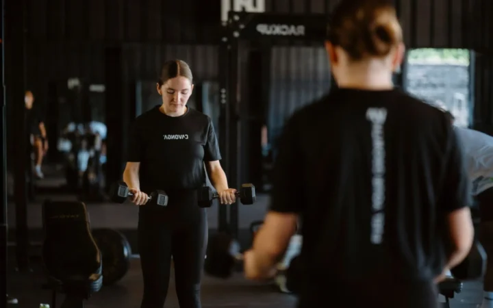 Woman performing a focused dumbbell workout in a modern gym setting.