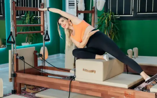 Woman practicing pilates on a reformer machine in a fitness studio, showcasing strength and flexibility.