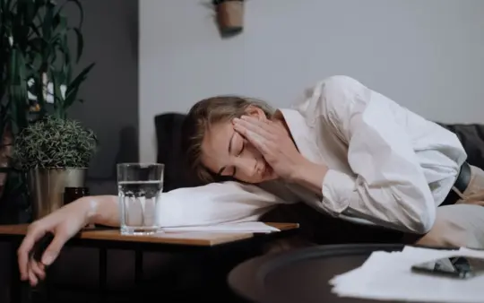 Tired woman in business attire resting with her head on a table in a cozy home setting.
