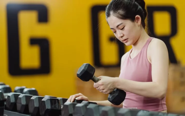 Young woman lifting dumbbell in gym, focusing on strength training with sports equipment.