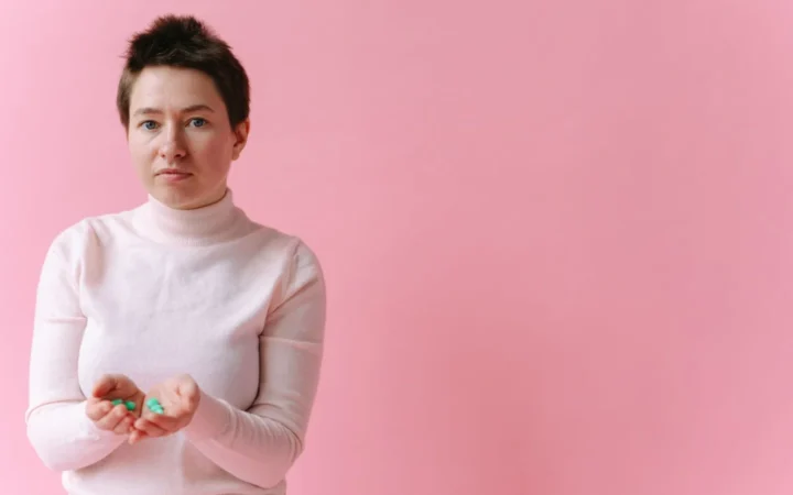 Caucasian woman holds pills in her hands against a soft pink backdrop, conveying healthcare themes.