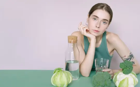 Young woman in a green top sitting with vegetables and a glass of water.