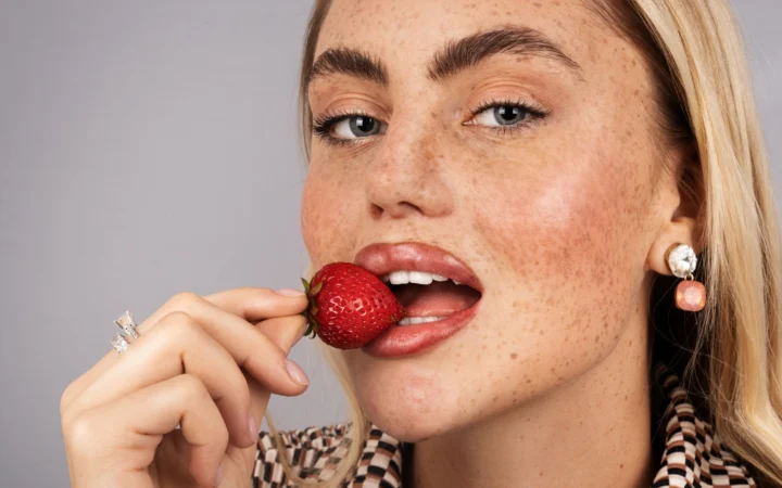 Close-up portrait of a blonde woman holding a strawberry near her lips.