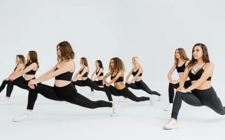 Group of women in black activewear performing lunges in a bright indoor studio, promoting fitness.