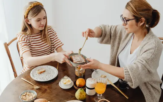Mother and daughter enjoying a cozy breakfast with toast and juice at the dining table.