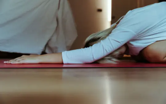 Young female practicing yoga at home wearing casual clothes and stretching body while doing extended child asana during