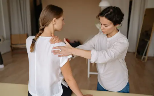 Therapist performing a shoulder massage on a woman to relieve physical tension.