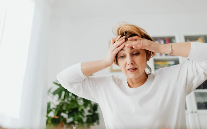 Worried woman indoors with hands on forehead, expressing stress.